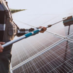 Technician cleaning rooftop solar panels with a soft brush to restore energy output