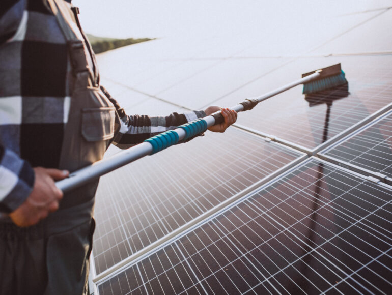 Technician cleaning rooftop solar panels with a soft brush to restore energy output
