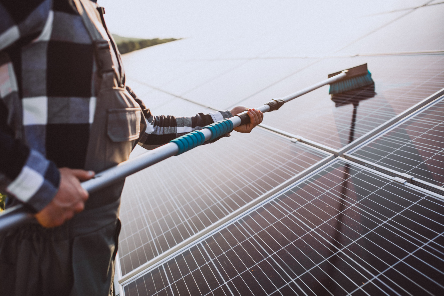 Technician cleaning rooftop solar panels with a soft brush to restore energy output